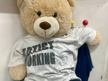 Teddy Bear wearing the Artist Working T-shirt and black leggins posig in a relax position. This is Bob our art assistant for our children classes.