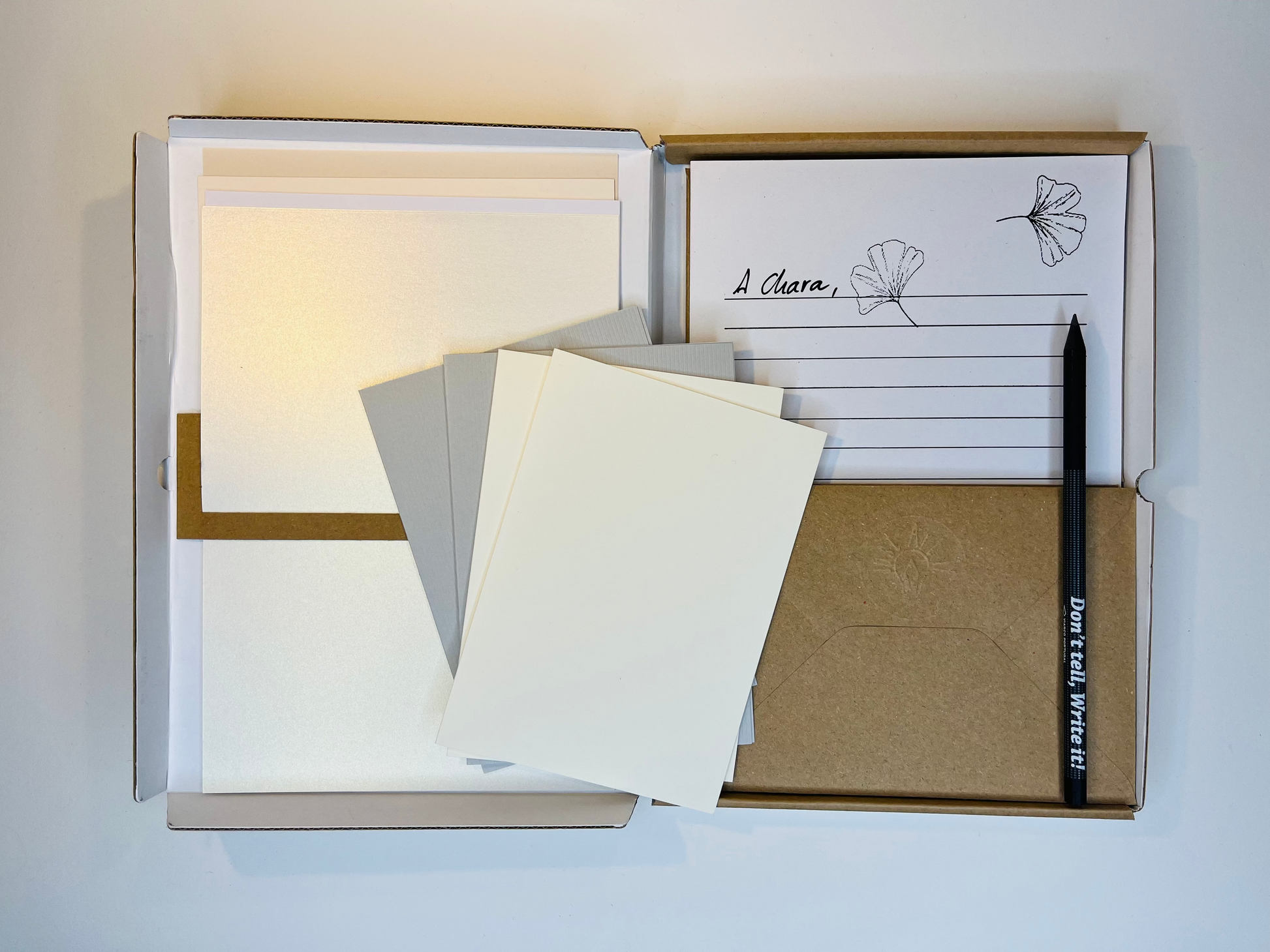 Open stationery box with various card stocks, envelopes, and pencil.