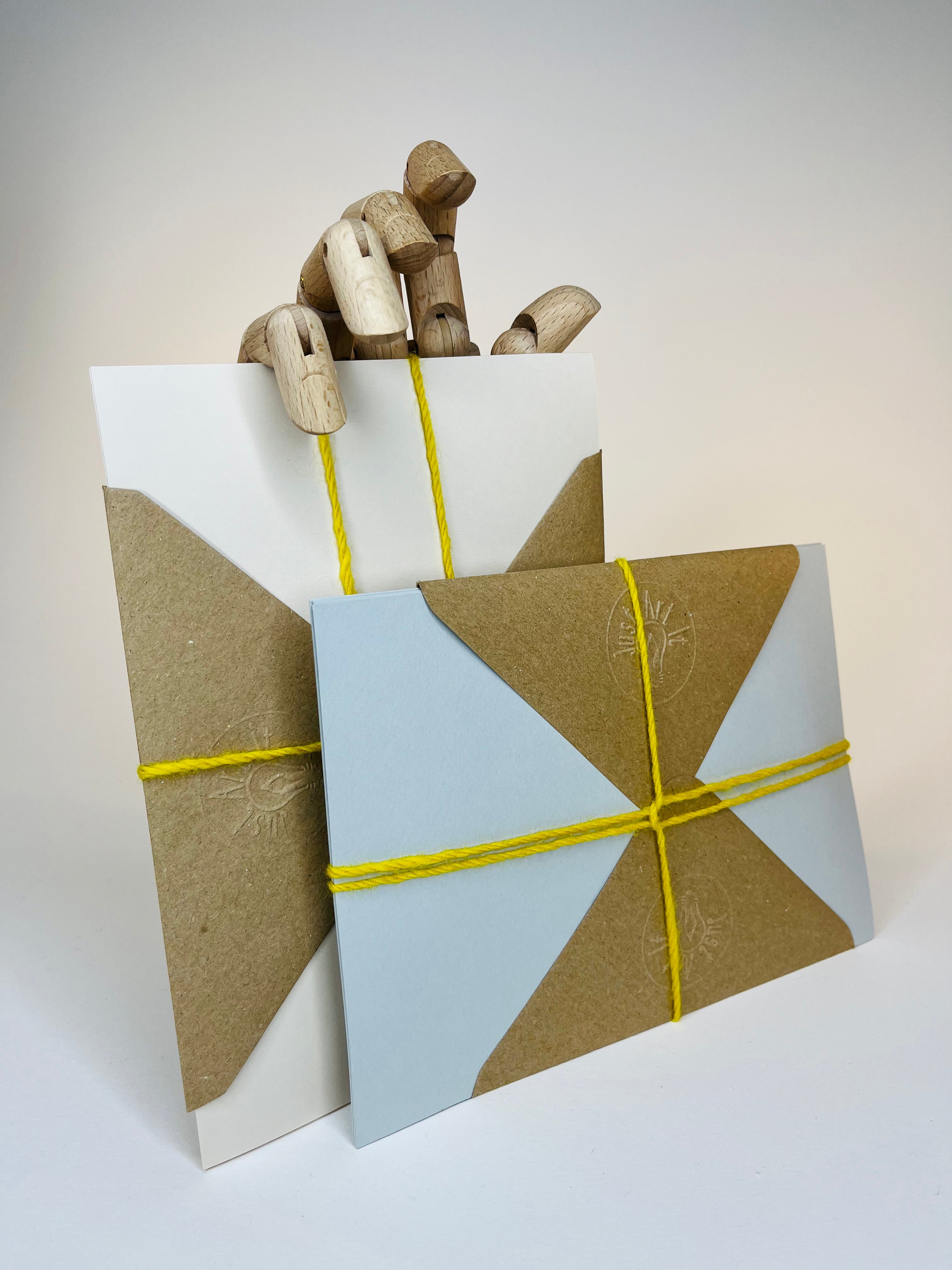 Two wrapped gift cards with a wooden mannequin hand peeking behind the tallest card.