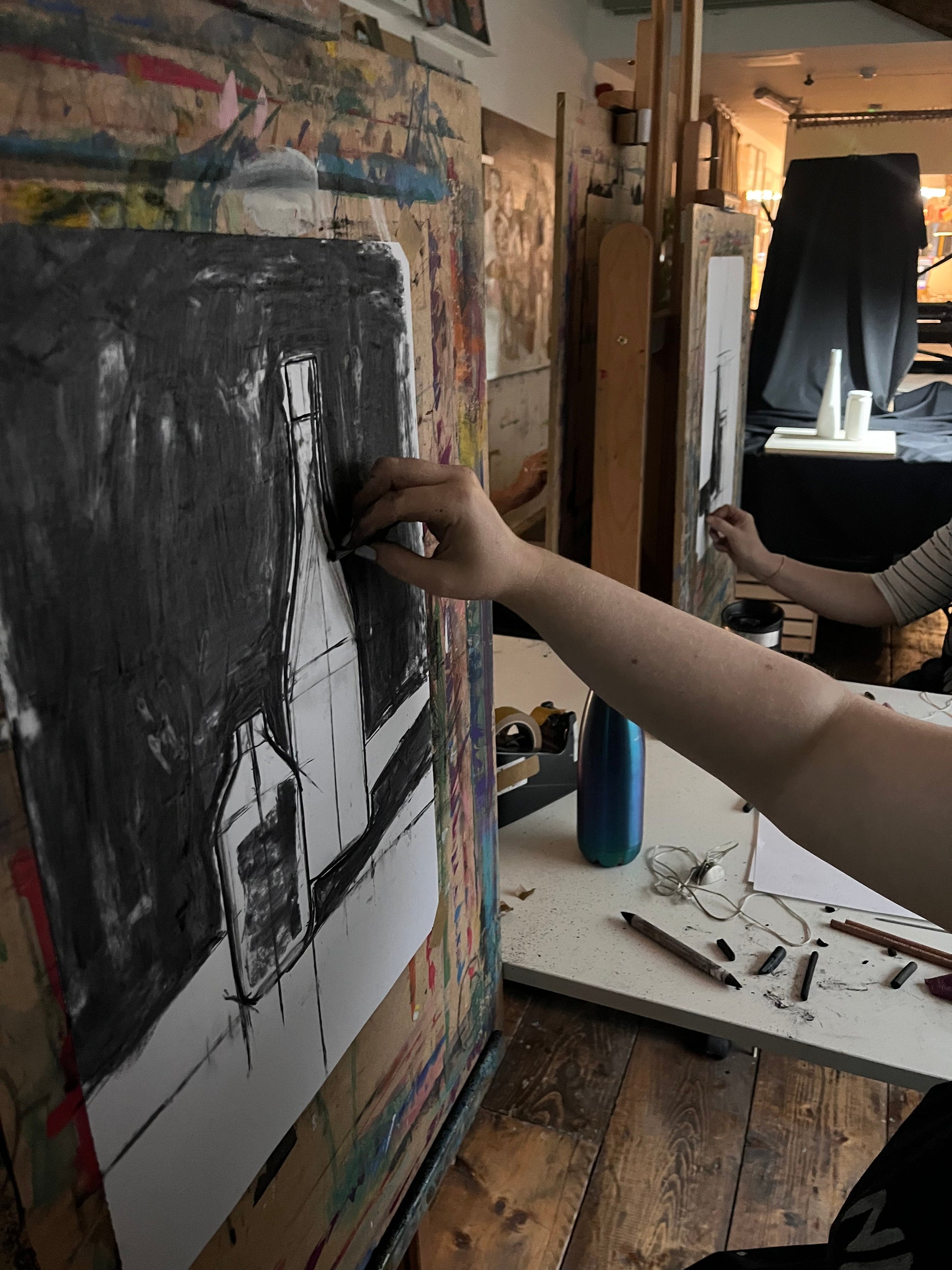 A person drawing a still life composition on paper using charcoal.