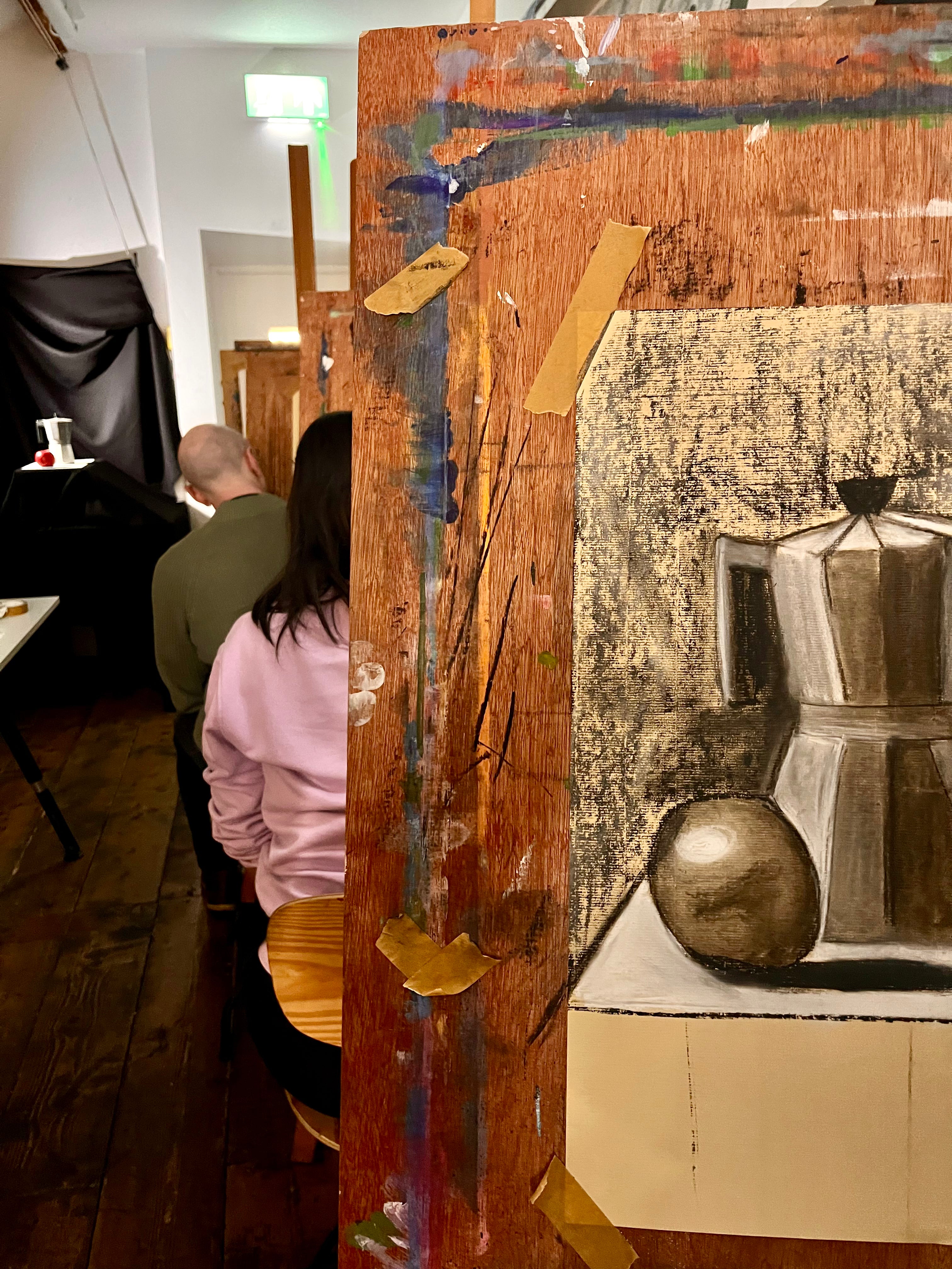 Artistic depiction of a still life scene on a wooden panel with visible wear in a classroom setup.