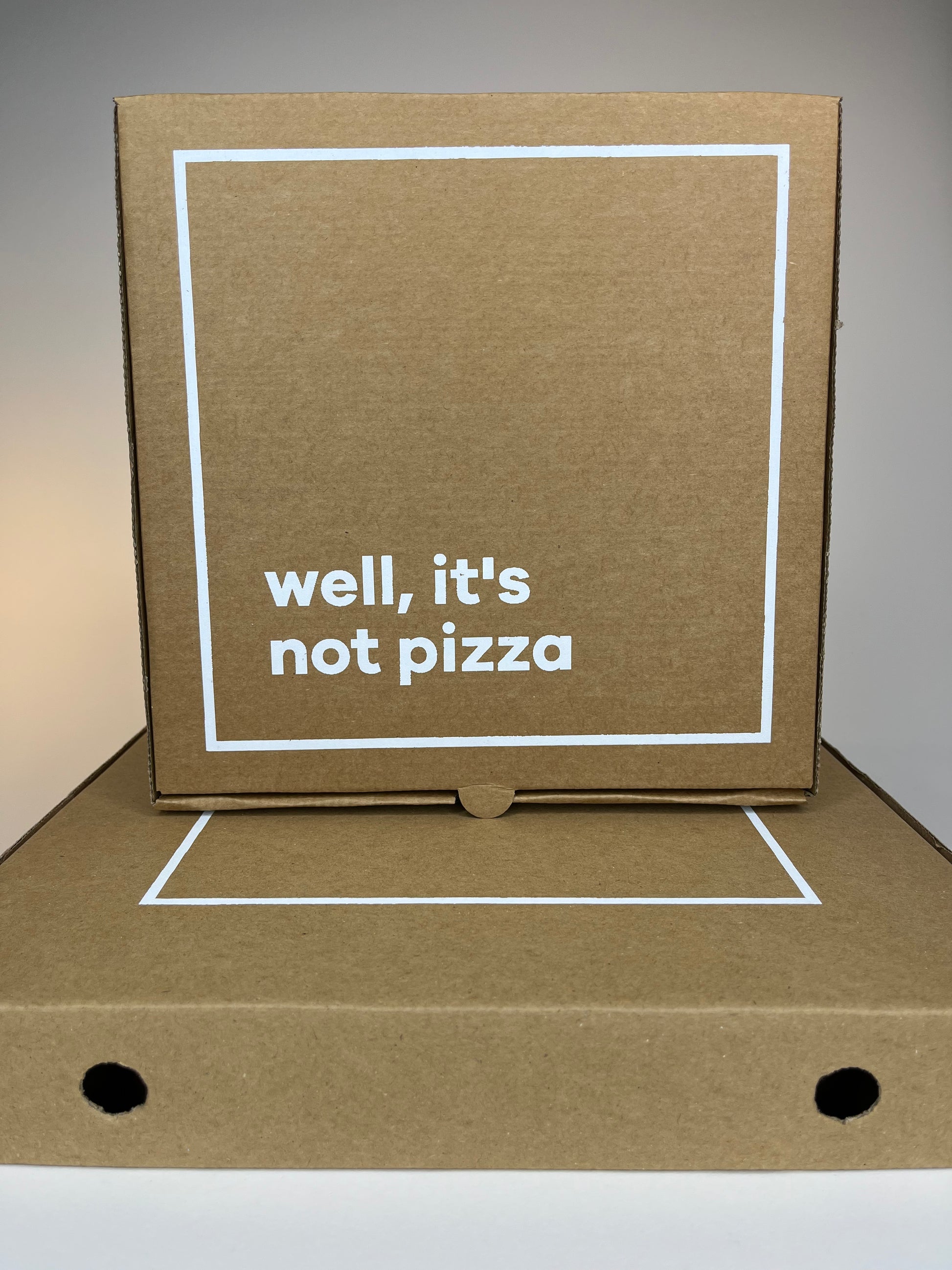 Two stacked brown cardboard boxes with white borders, one with the text "well, it's not pizza."