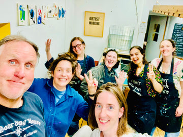 Group of people in a studio setting, some wearing aprons, with a casual and friendly atmosphere.