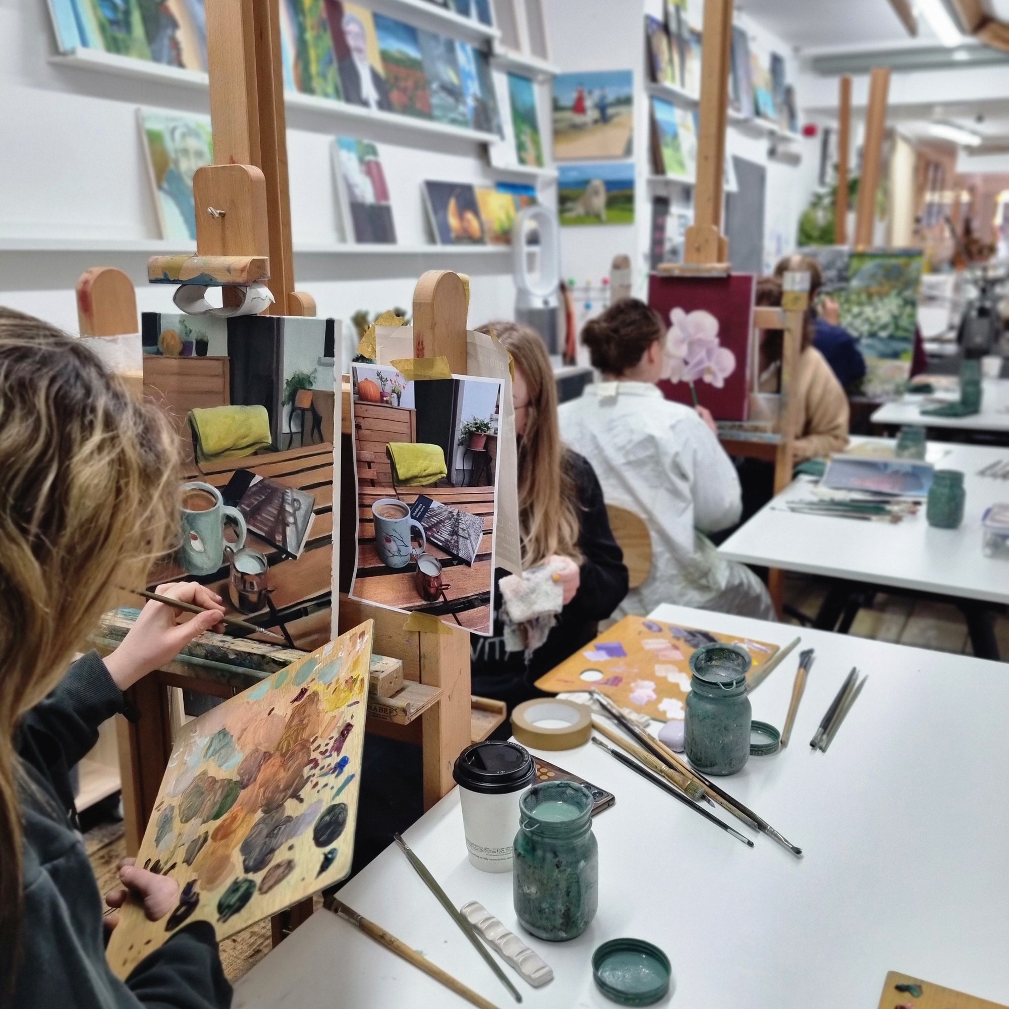 Art studio with students painting at easels and tables.