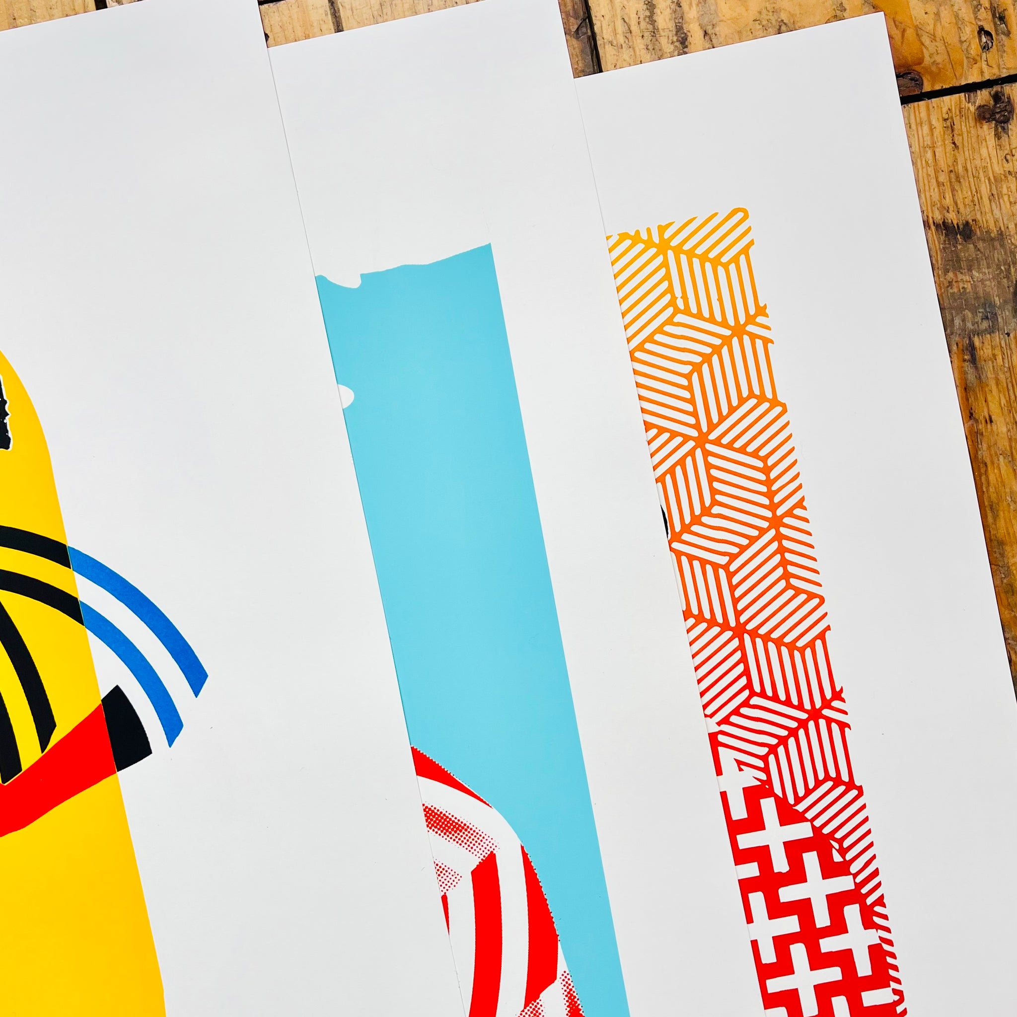 Three colorful abstract art prints on a wooden surface