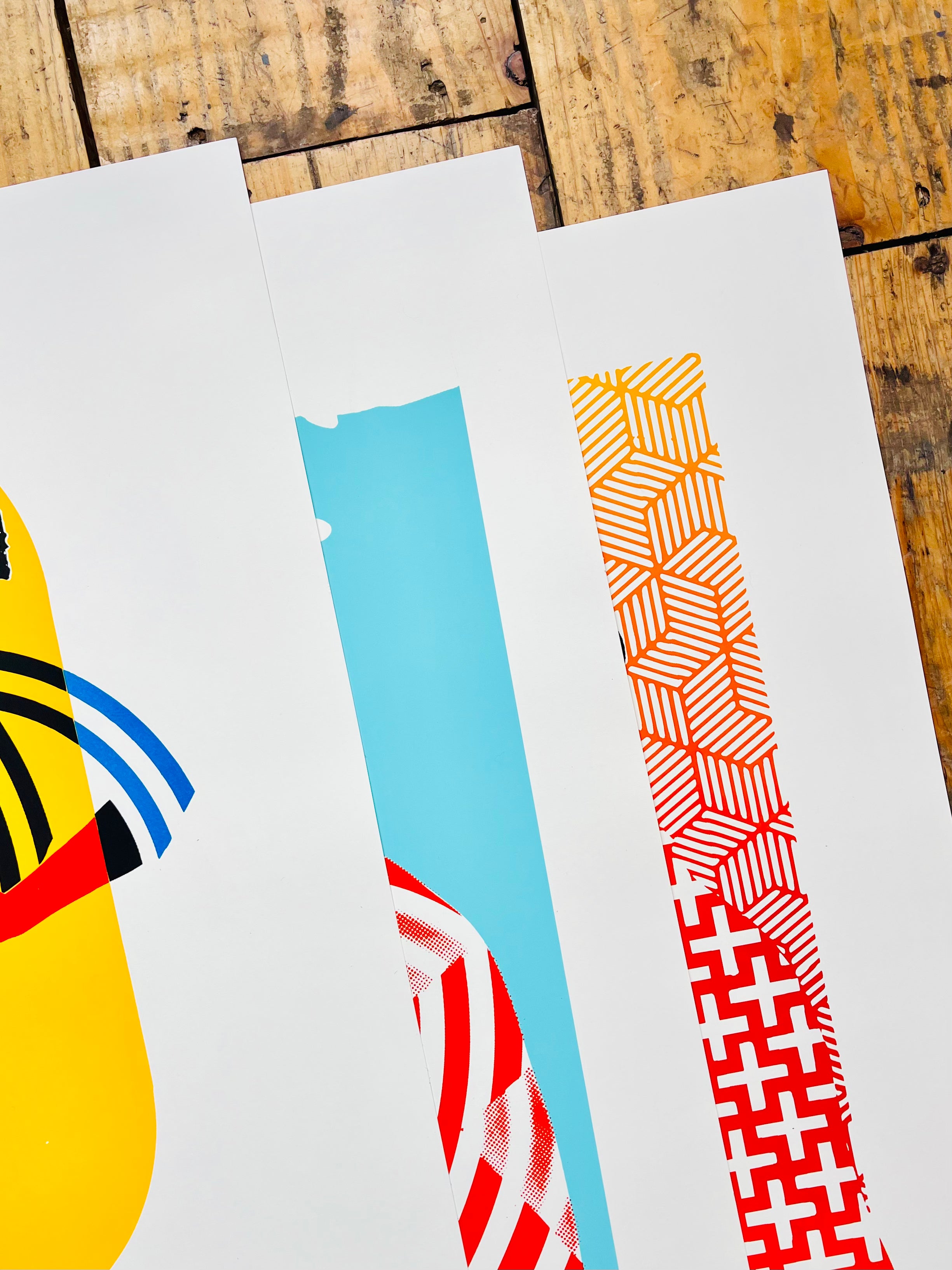 Three colorful abstract art prints on a wooden surface