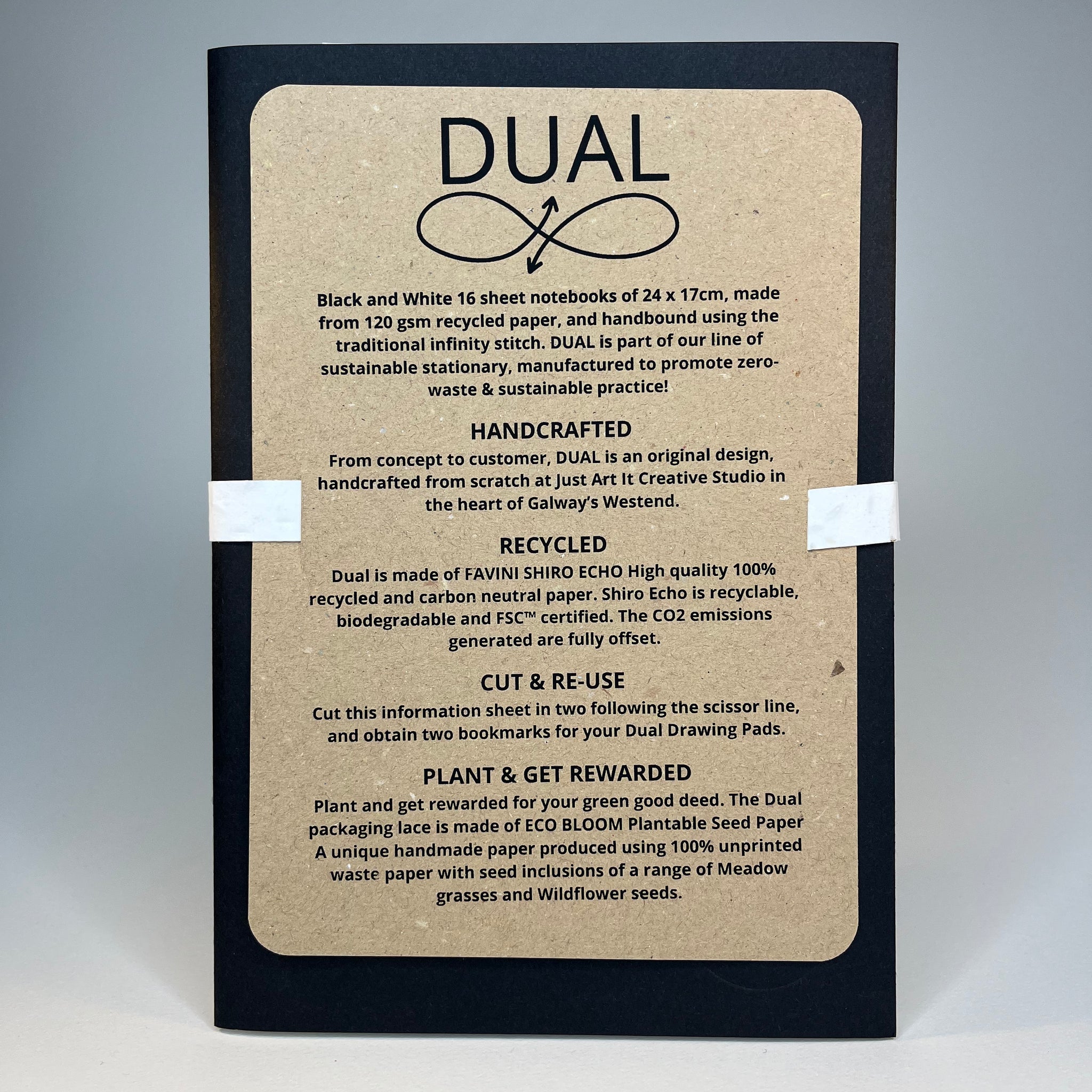Close-up of a black notebook with a brown recycled paper cover featuring the word "DUAL" and sustainability information.