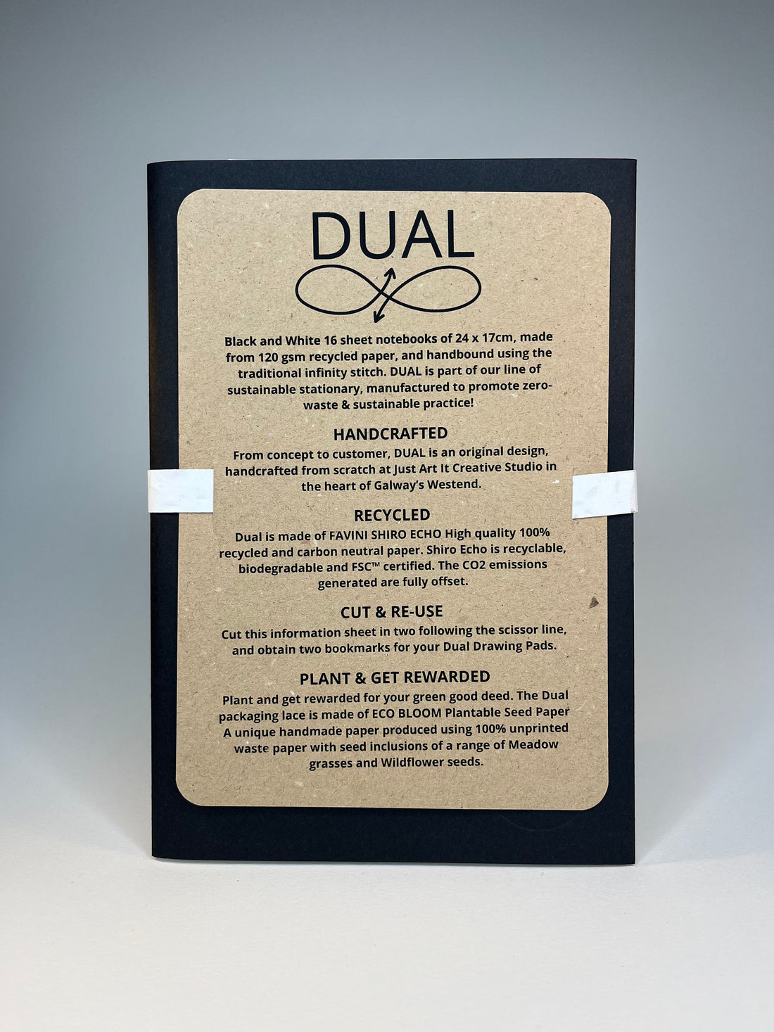 Close-up of a black notebook with a brown recycled paper cover featuring the word "DUAL" and sustainability information.
