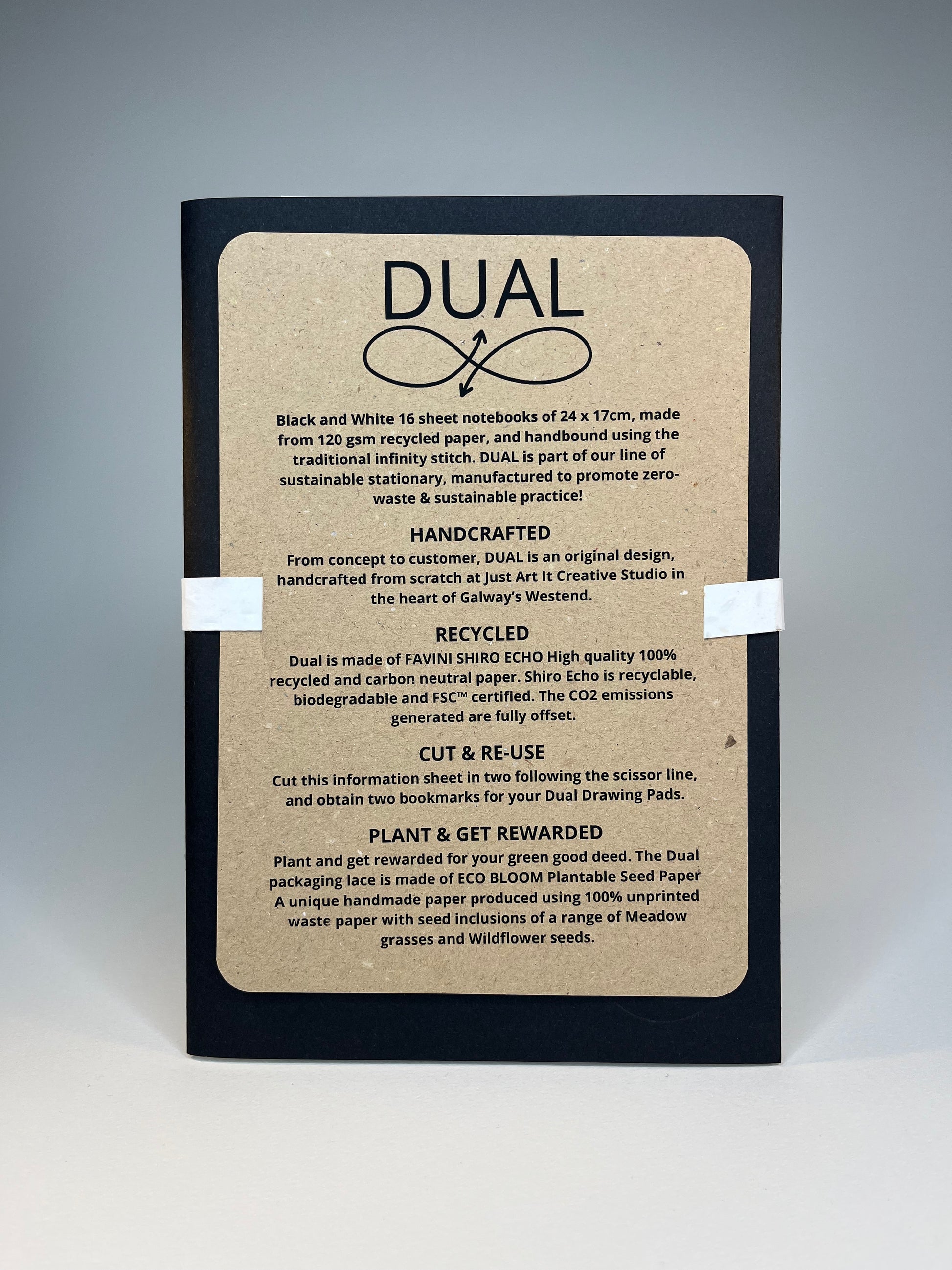 Close-up of a black notebook with a brown recycled paper cover featuring the word "DUAL" and sustainability information.
