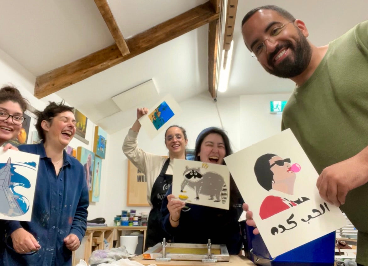 Group of people laughing at Just art It workshop holding up their prints on the last day of their course.  