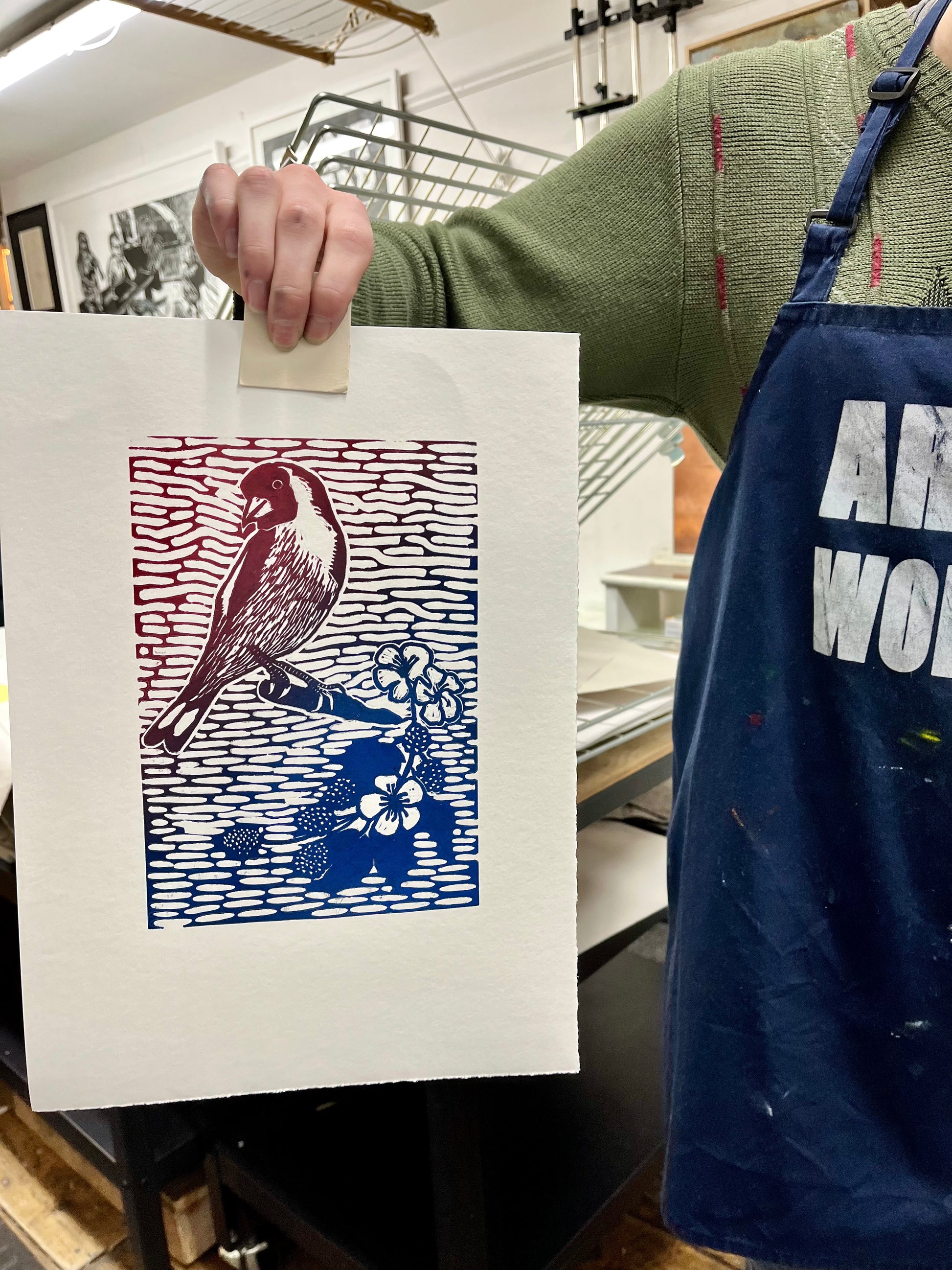 Person holding a print with a bird design, wearing an apron.