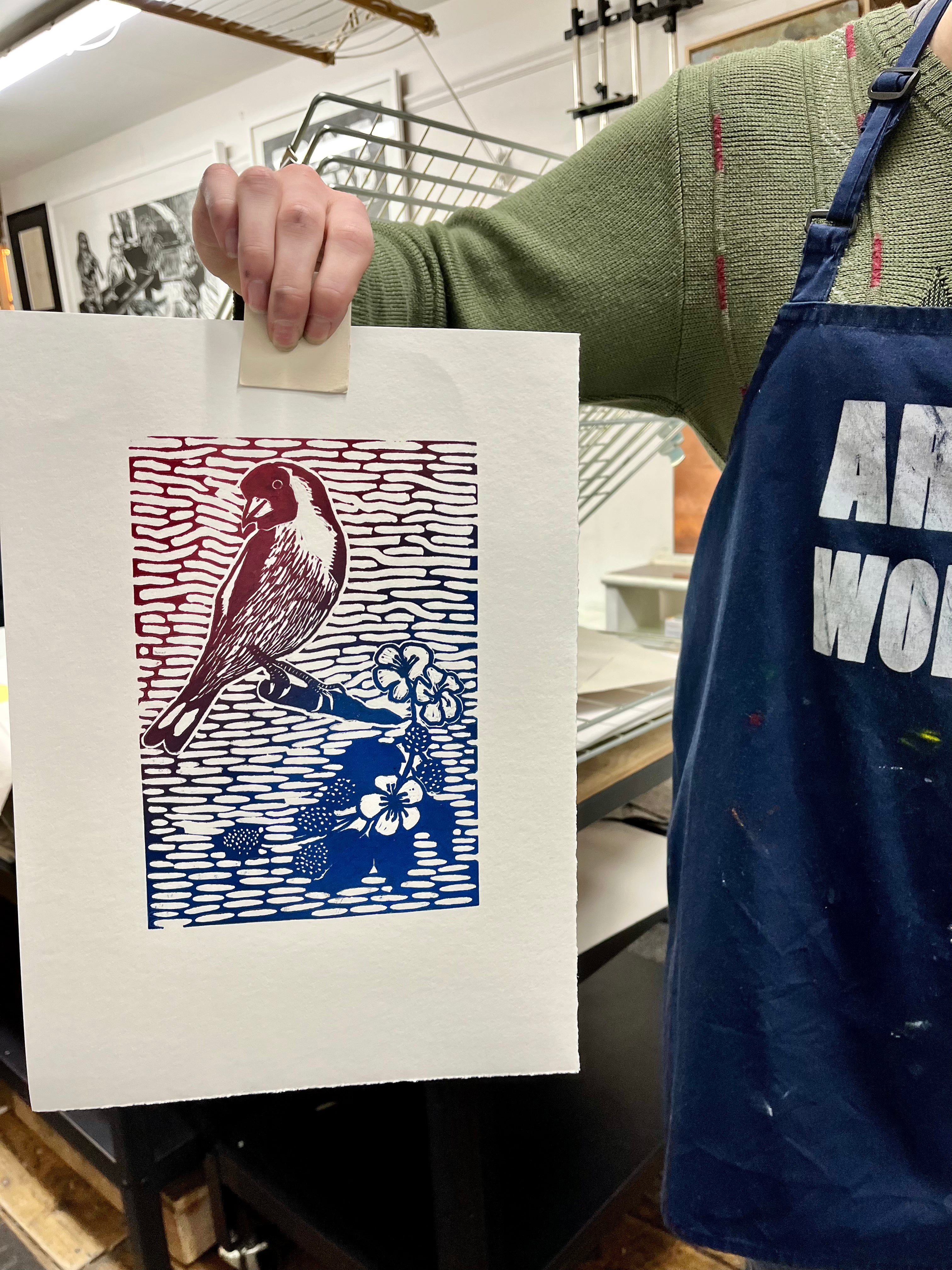 Person holding a print with a bird design, wearing an apron.