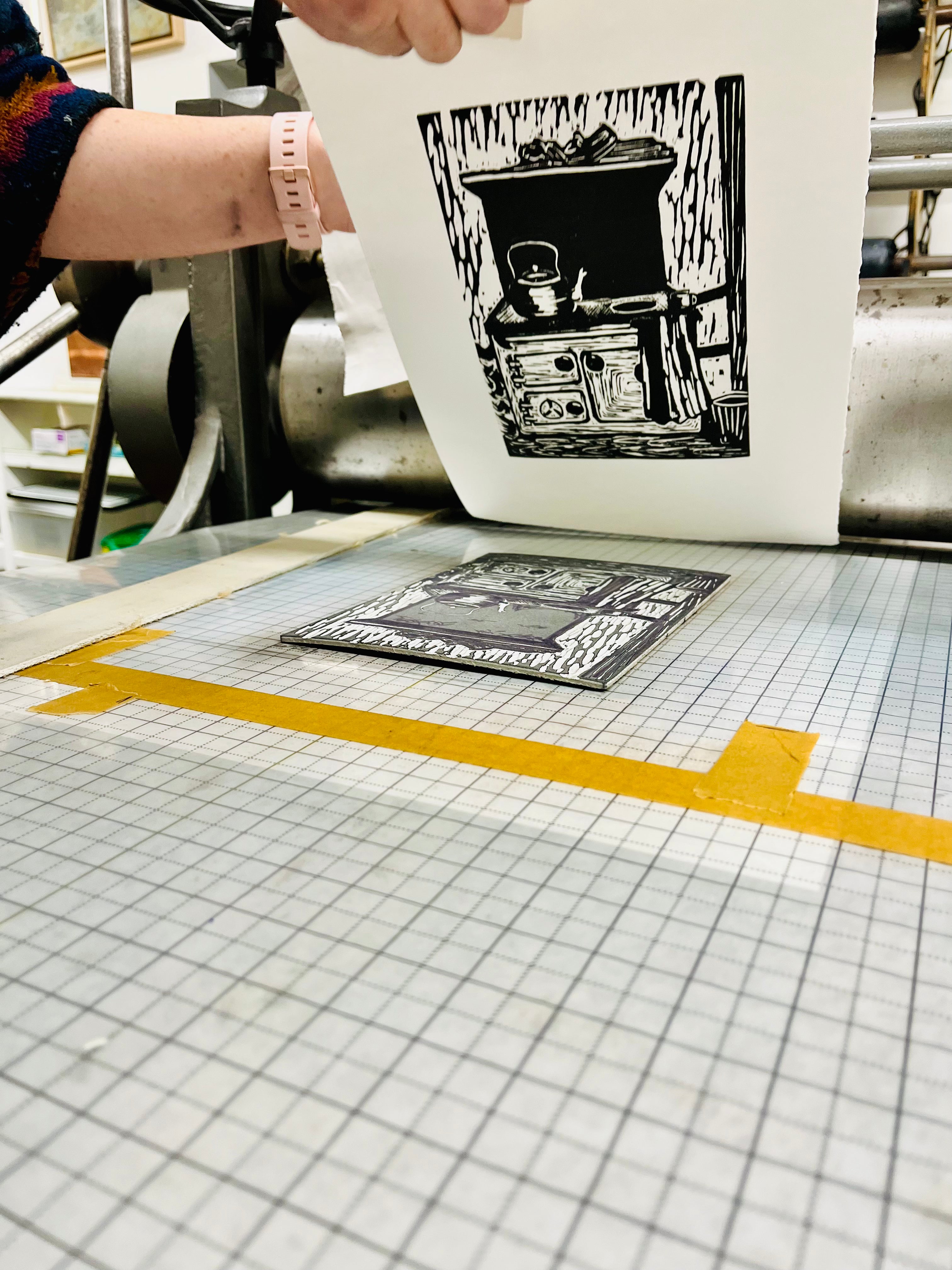 Person holding a print of a black and white illustration on a printing press table.