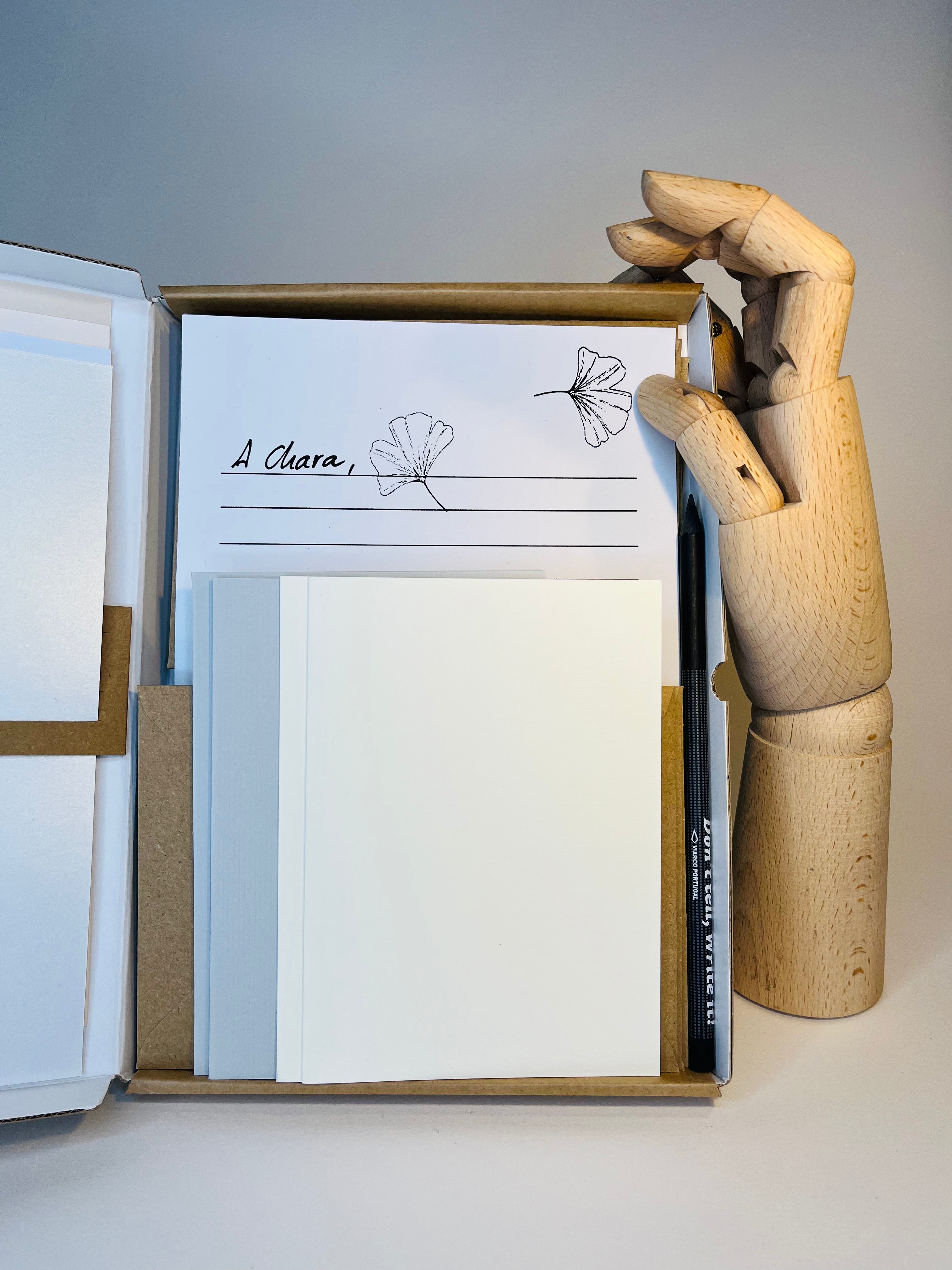 Open stationery set with white and blue notecards, a pen, and a wooden artist's hand, presented on a white surface.
