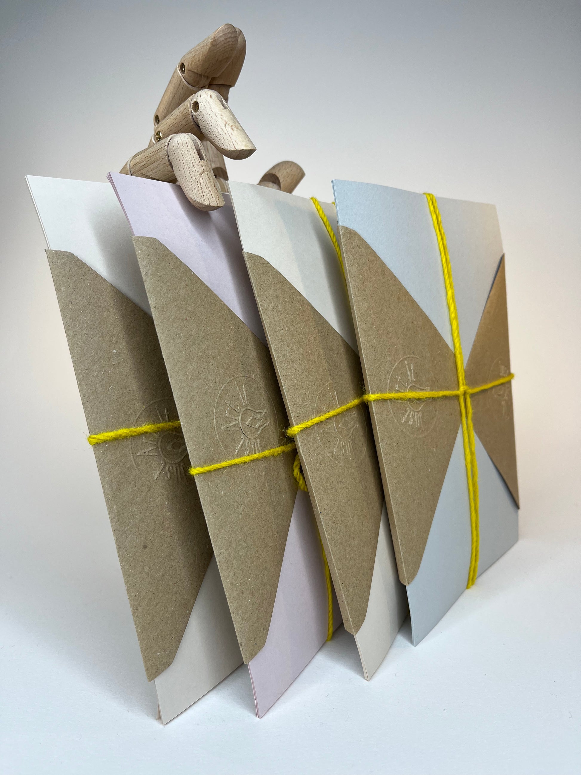 Four color-blocked envelopes secured with yellow string and "held" by an articulated wooden figure.