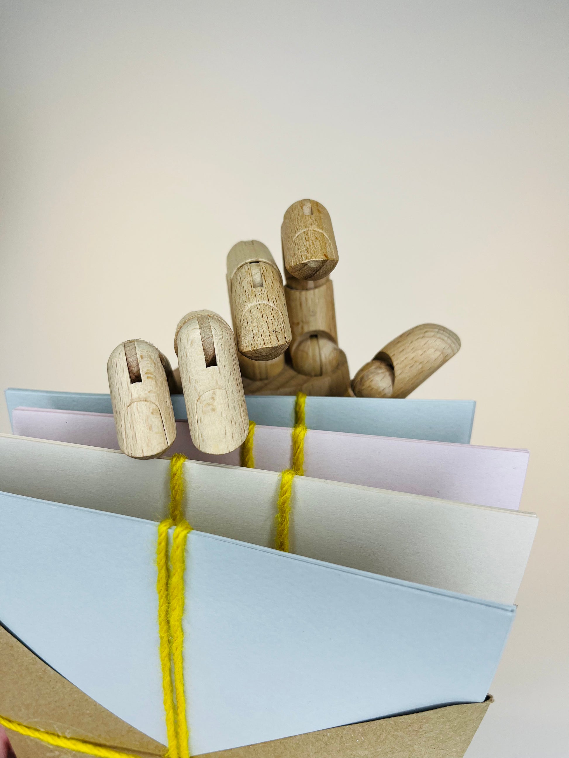 Wooden hand model holding pastel envelopes tied with yellow yarn.