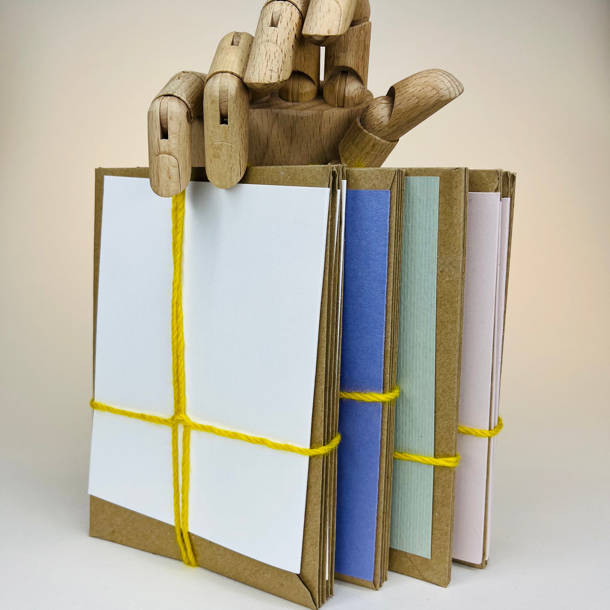 Wooden hand holding a stack of tied, colorful envelopes.