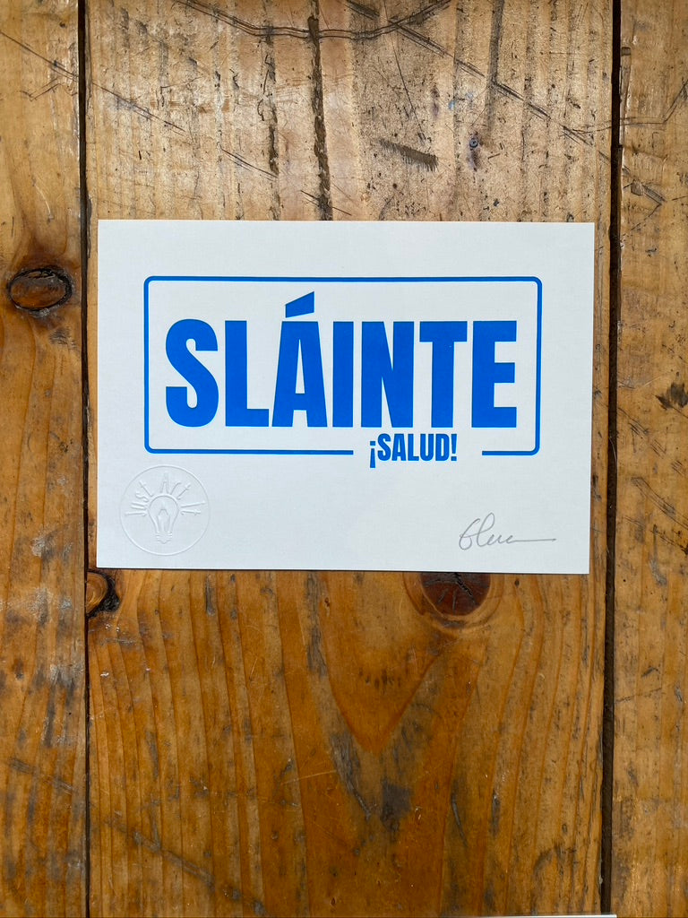 Screen print on white paper with 'SLÔINTE á SALUD!' text on a wooden surface