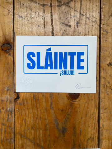 Screen print on white paper with 'SLÔINTE á SALUD!' text on a wooden surface