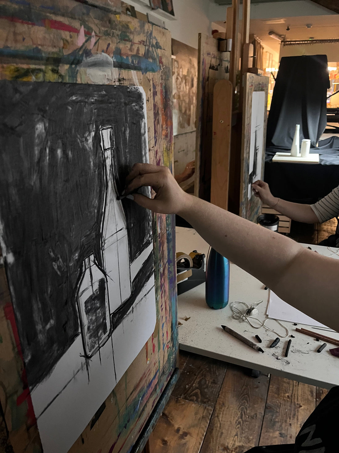 A person drawing a still life composition on paper using charcoal.