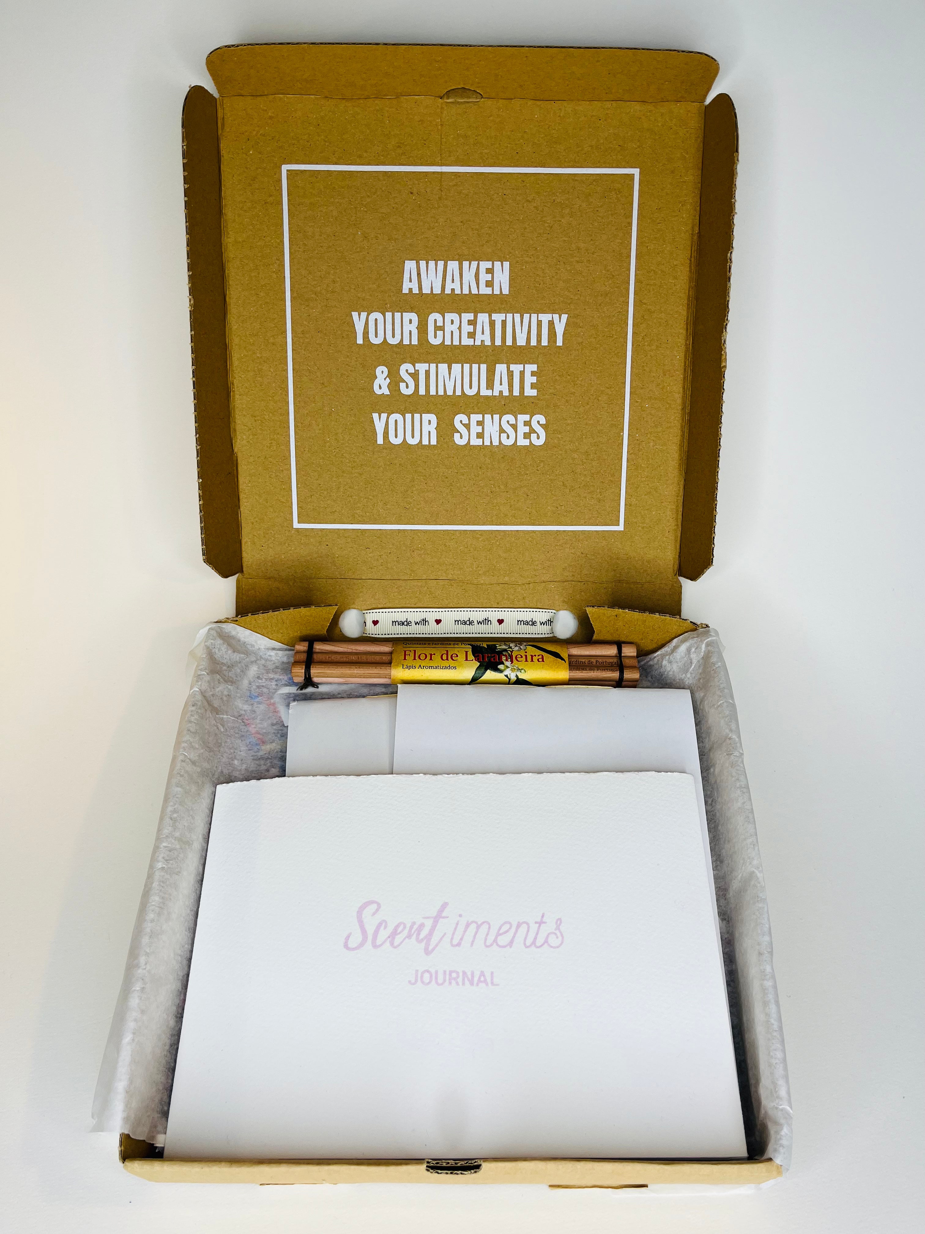 Open box containing a journal, pencils, and ribbon.