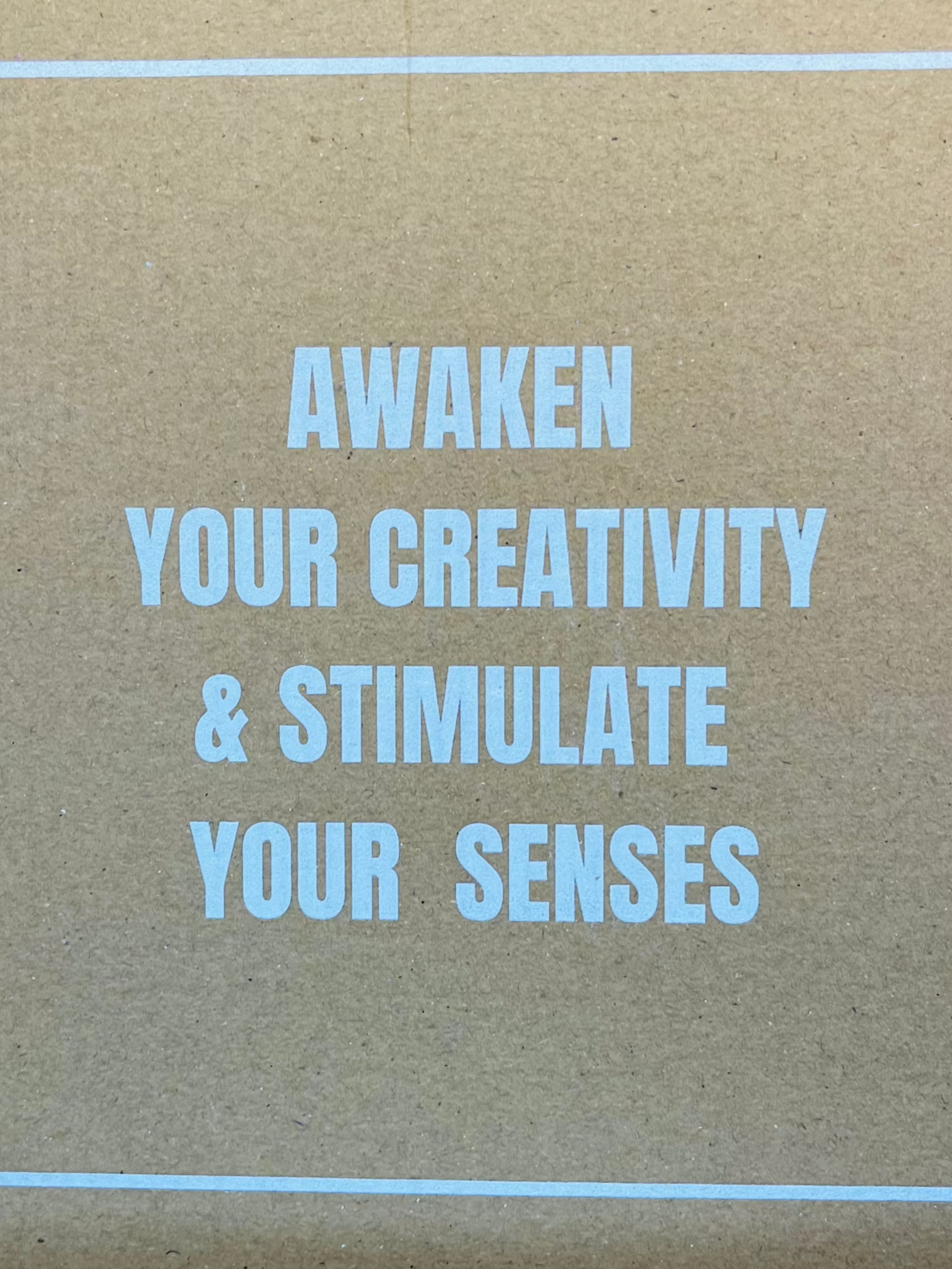 Tan surface with blue sans-serif text: "AWAKEN YOUR CREATIVITY & STIMULATE YOUR SENSES". Thin blue lines at top and bottom.