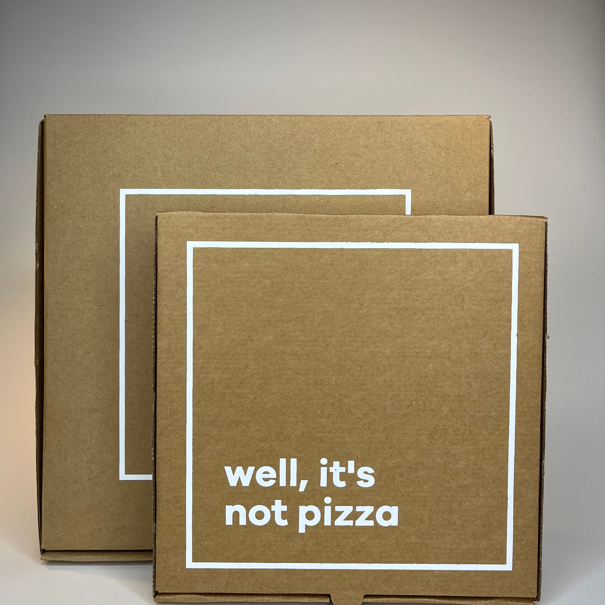 Two brown cardboard boxes with white square borders, one displaying "well, it's not pizza" in white text.