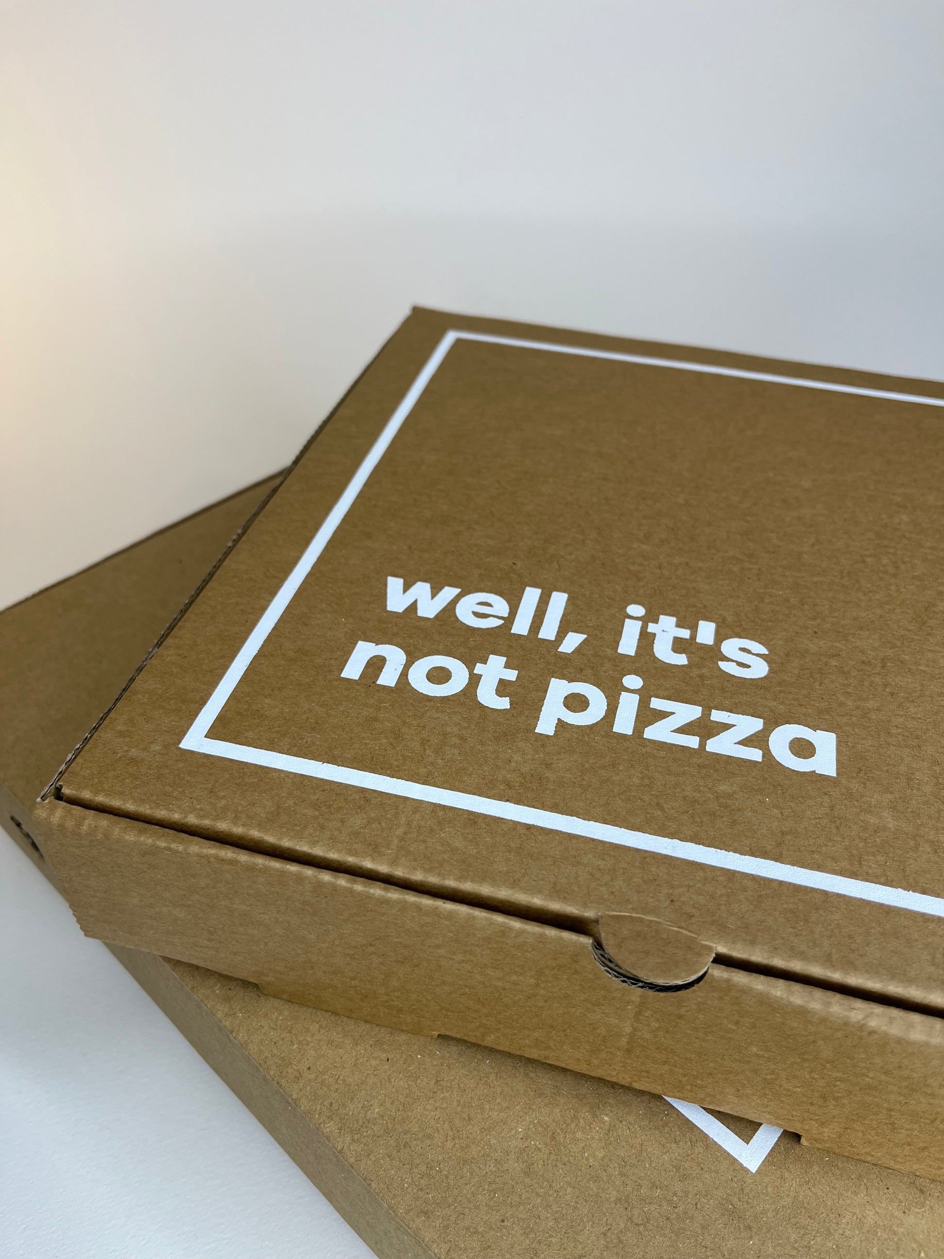 Two stacked, brown cardboard boxes with the text "well, it's not pizza" inside a white border.