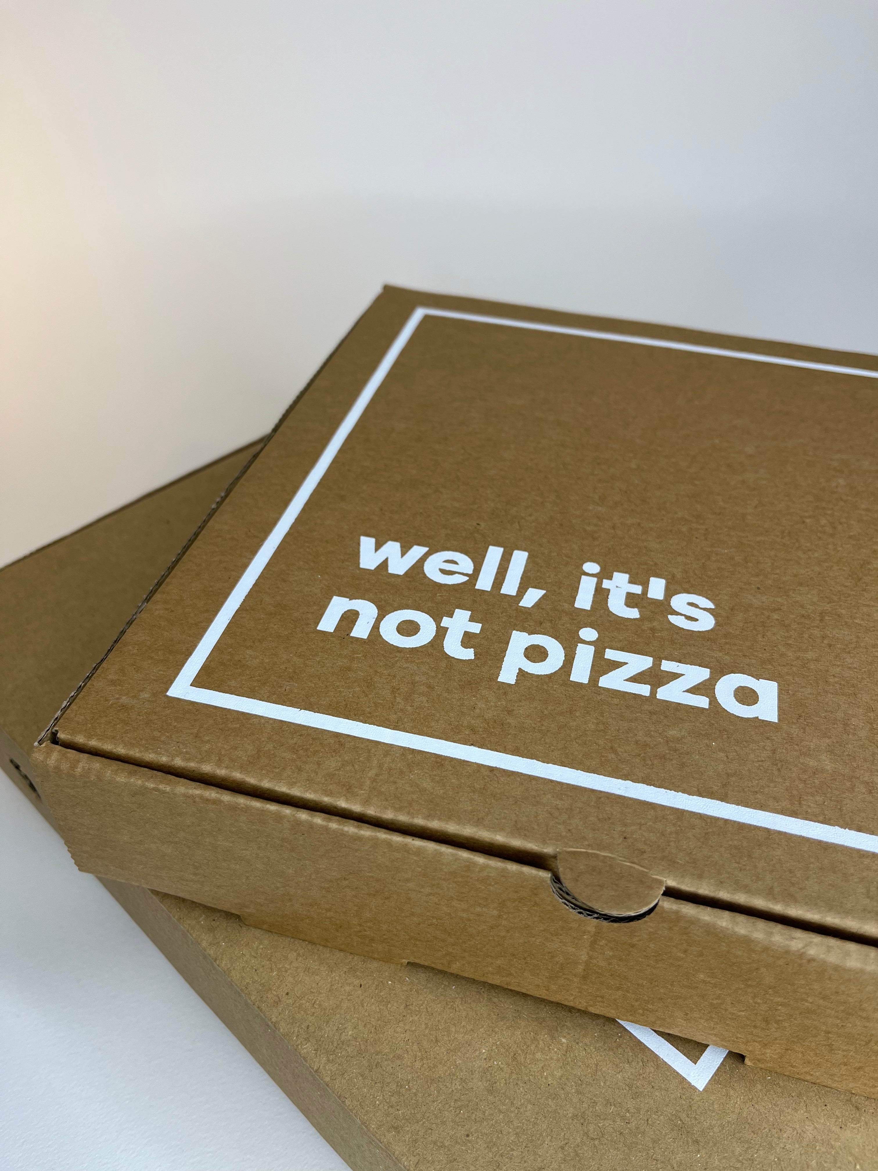 Two stacked, brown cardboard boxes with the text "well, it's not pizza" inside a white border.