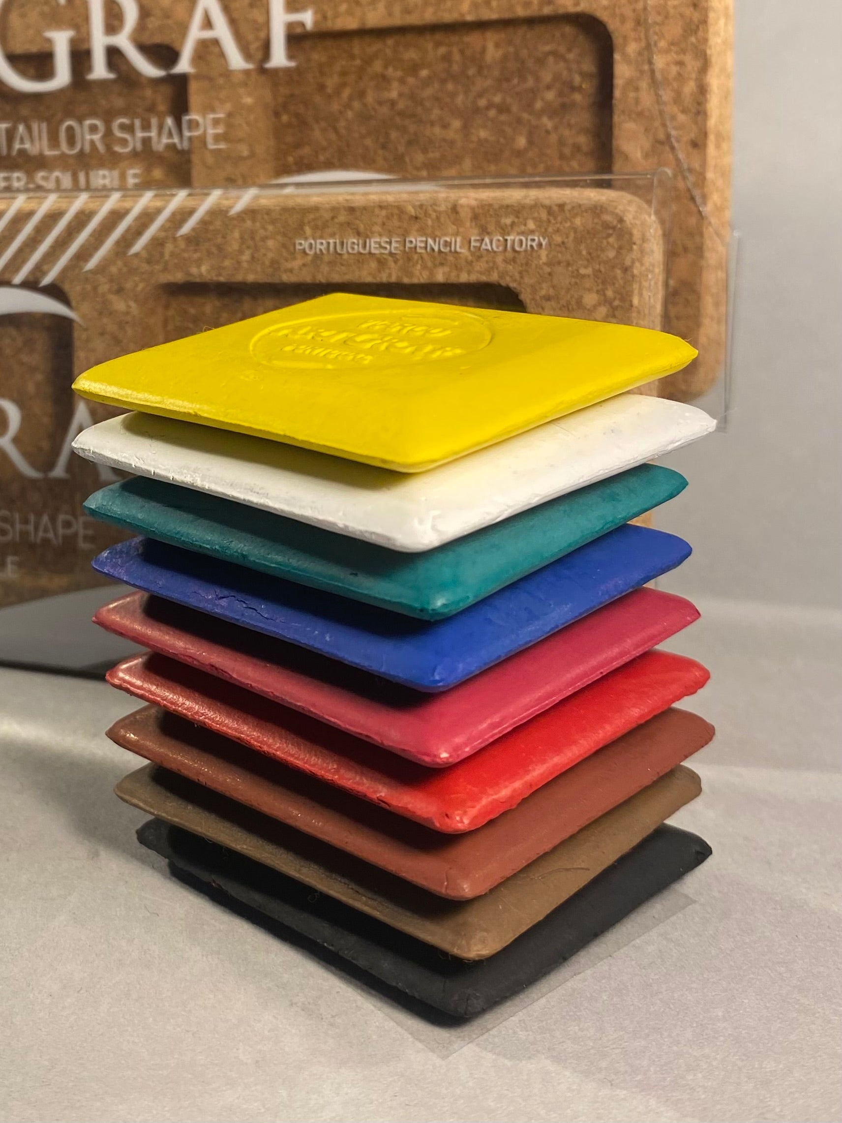 Stack of colorful square coasters with a branded pencil box in the background.